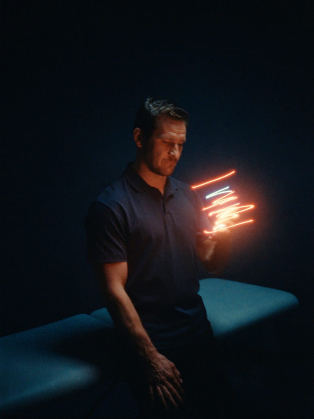 Een kinesist in zijn behandelruimte kijkt naar zijn telefoon die oplicht.